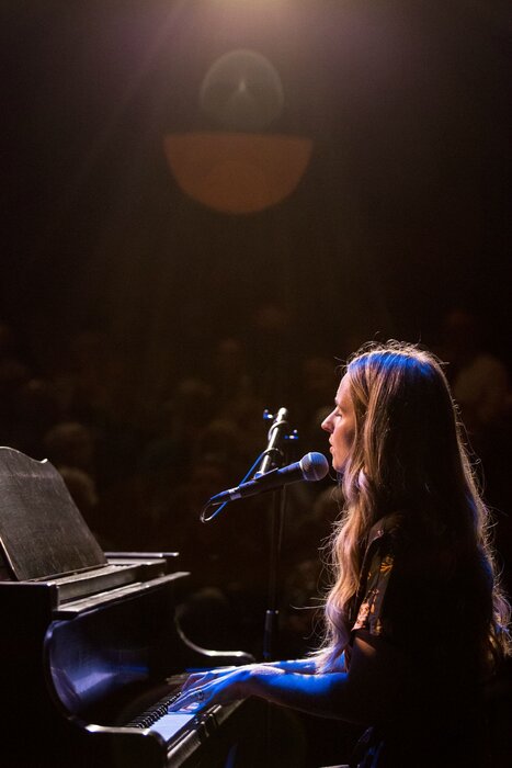 Illuminated by a spotlight, Alex Mundy plays piano in a concert setting.