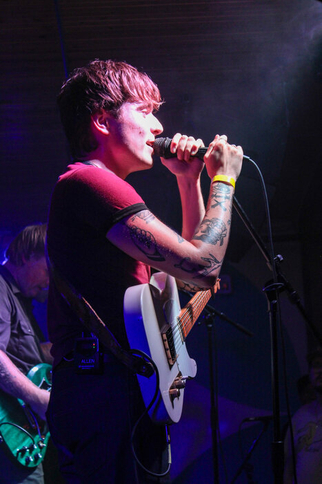 The lead singer of Arm's Length holds a microphone with both hands while singing at Broom Factory in Kingston.